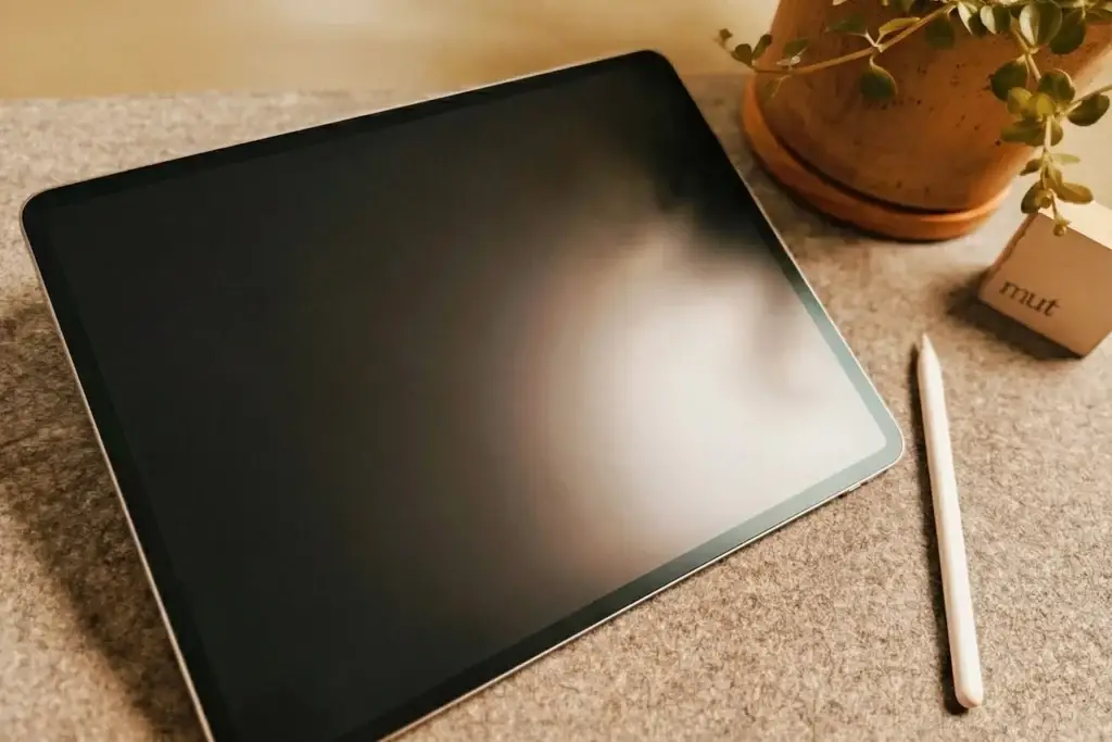 „iPad mit Stift auf Filzunterlage neben einer Pflanze – warmes, ruhiges Stillleben für die Coaching-Website karrierefarben.“